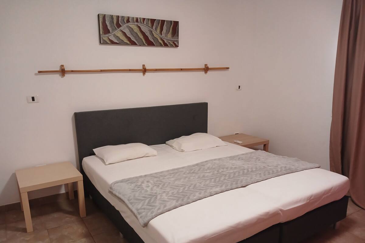 A neatly arranged bedroom with a bed, two bedside tables, a wall-mounted artwork, and a curtain.