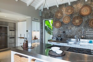 Une cuisine moderne dotée d’un îlot central, d’appareils électroménagers en acier inoxydable et d’un pare-feu en pierre.