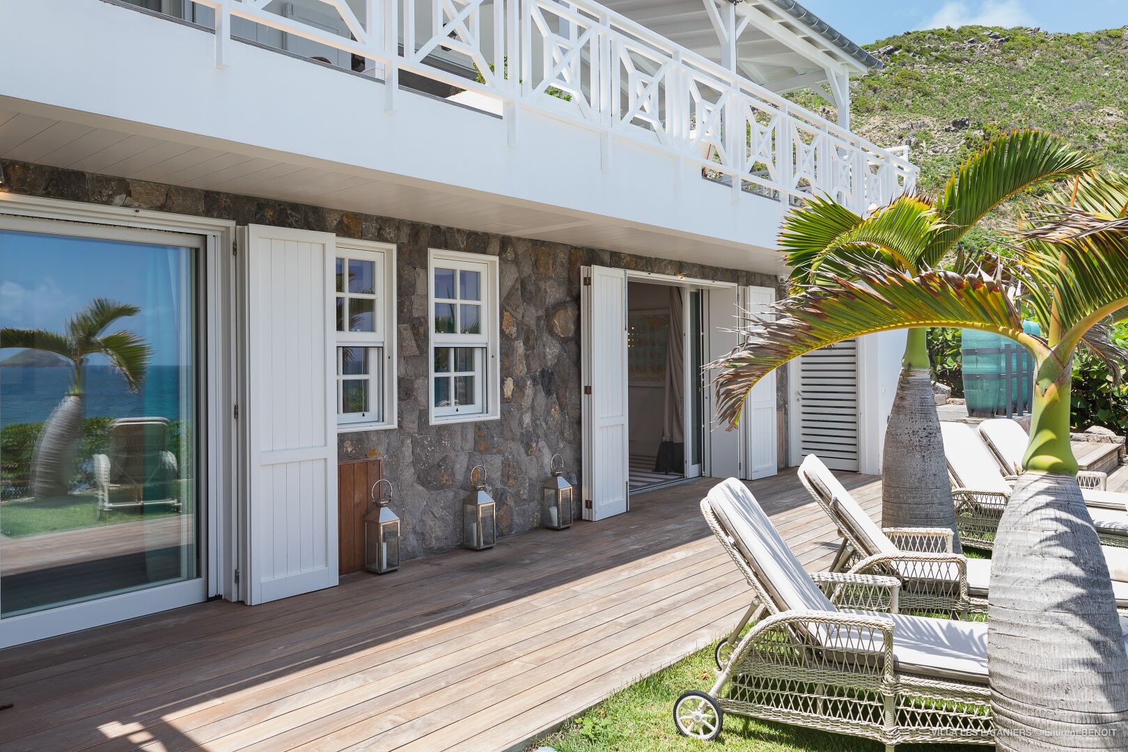 A modern house with a wooden deck, white exterior, and a view of the ocean.