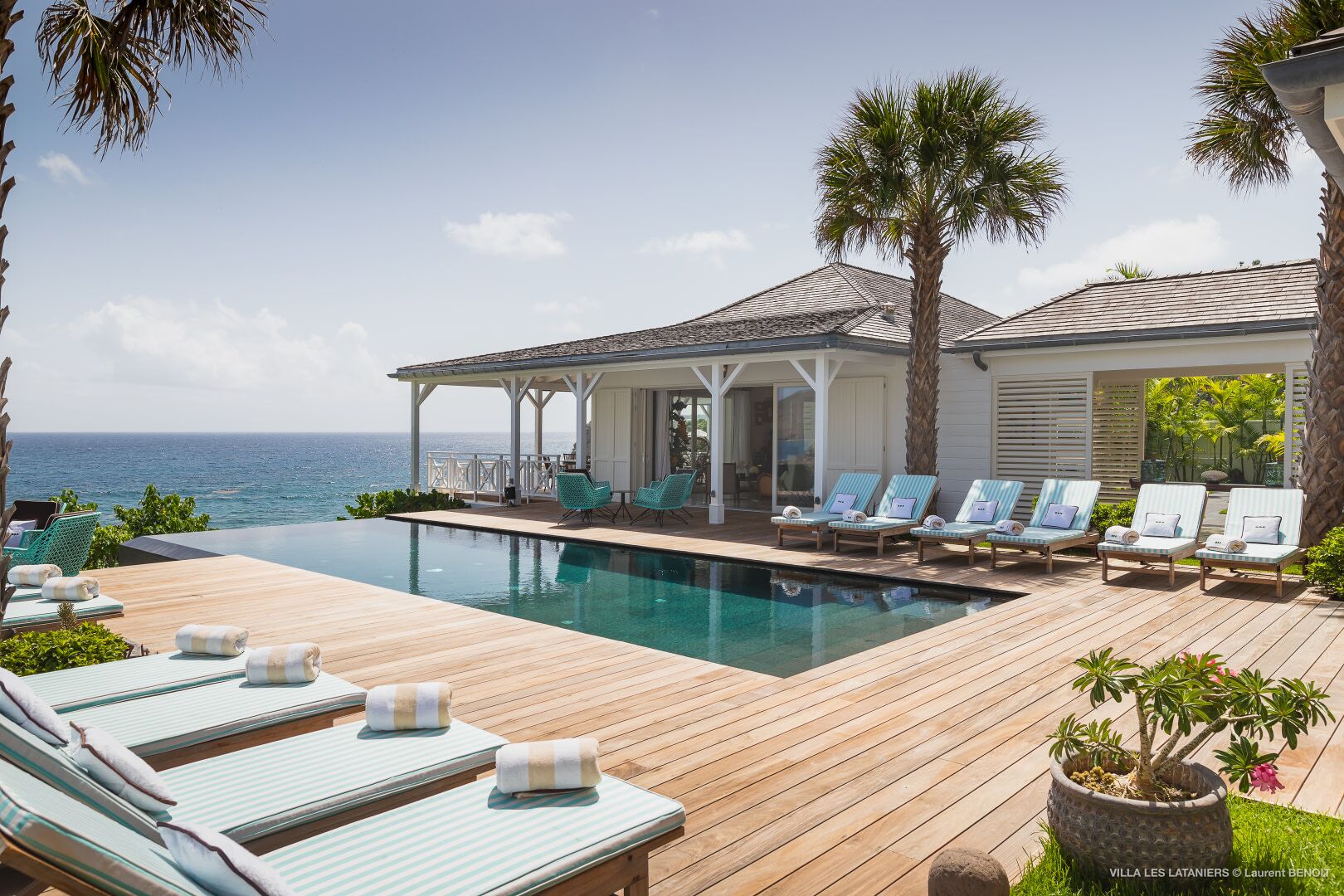 Un espace aménagé au bord de la piscine, avec des chaises longues, un coin salon abrité et une vue sur l’océan.
