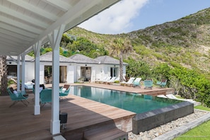 Un espace aménagé au bord de la piscine, avec des chaises longues, une terrasse en bois et une vue sur une colline.