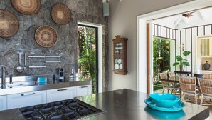 Een moderne keuken met een groot eiland, een steen rugpaneel en een eethoek met rieten stoelen.