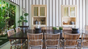 A dining area with a dark wooden table and wicker chairs, flanked by two wooden cabinets with striped glass doors.