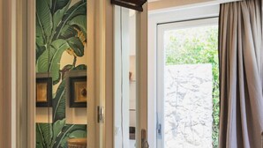 A hallway with a door leading to a balcony, a tropical-themed wall mural, and a wicker chair.