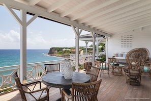 A covered outdoor seating area with wicker furniture and a view of the ocean.