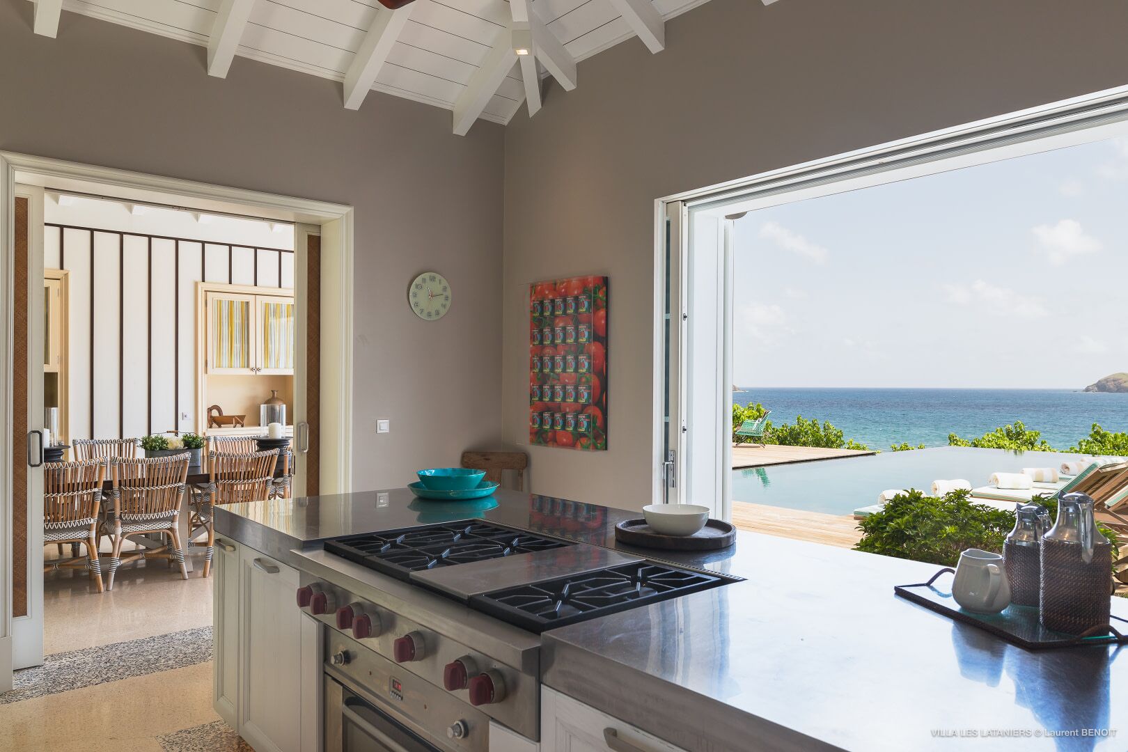 A kitchen with a view of the ocean, a dining area with wicker chairs, and a modern stove.