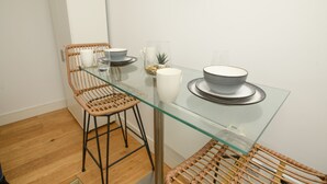 Ein Essbereich mit einem Glastisch, zwei Korbstühlen, einem weißen Schrank und einem an der Wand befestigten Regal mit Dekoration.