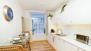 Eine kleine Küche mit weißen Schränken, einer Mikrowelle und einem Toaster. Ein Esstisch mit Stühlen und ein Fenster mit Blick.