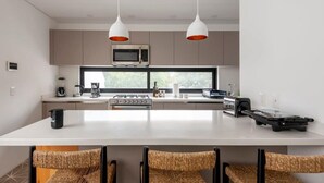 A modern kitchen with a central island, white pendant lights, and a view through the window. - w* | Inspiring 3BR Duplex with Terrace in Polanco (Ciudad de México)