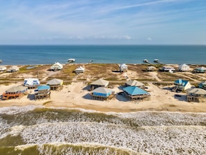 Eine Küstenlandschaft mit Strandgrundstücken und erhöhten Gebäuden, einige mit blauen Dächern, mit freiem Blick auf den Ozean.