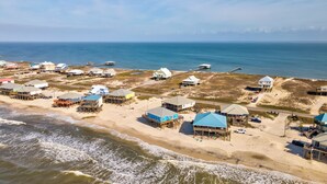 An aerial view of a coastal area with beach houses, some elevated on stilts, and a pier extending into the water. - Blue Sky Breeze - Gulf Front, Pet Friendly on the beach (Dauphin Island)