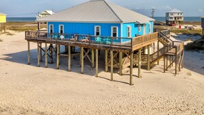 A blue building with a wooden deck and stairs, located on a sandy beach. - Blue Sky Breeze - Gulf Front, Pet Friendly on the beach (Dauphin Island)