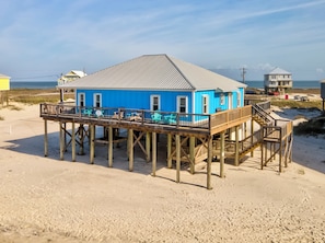 Ein blaues Gebäude mit einer Holzterrasse und Treppe, direkt an einem Sandstrand gelegen.