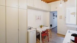 Una cucina compatta con mobili bianchi, un piccolo frigorifero, un tavolo con sedie e un soffitto in legno.