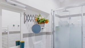 Ein modernes Badezimmer mit Glasdusche, weiß geflieste Wand mit grauen Akzenten, rundem Spiegel und Ablage mit Topfpflanze.