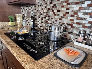 A kitchen with a black induction cooktop, a stainless steel pot, and a cutting board with carrots.