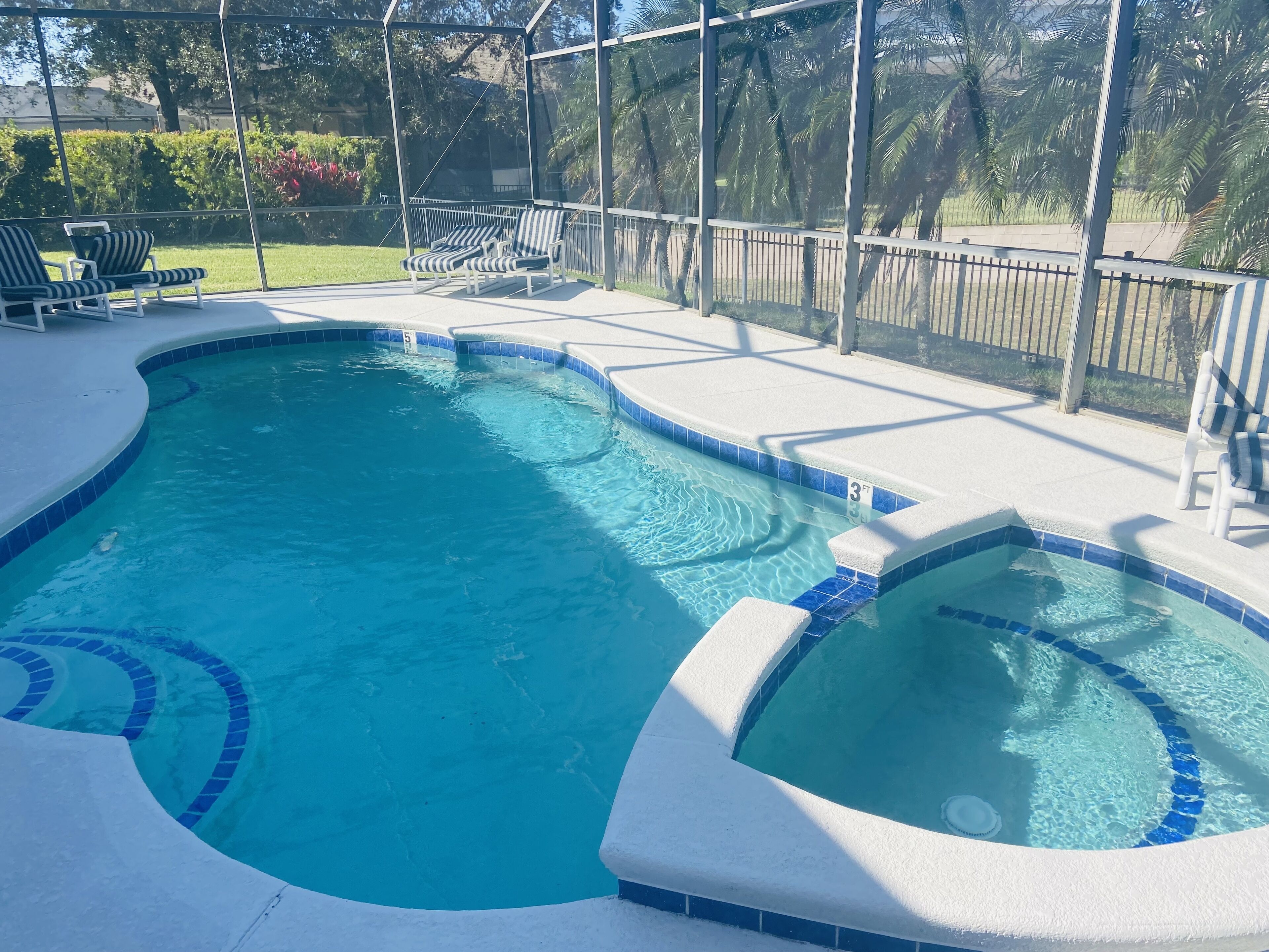 A swimming pool with a hot tub, surrounded by a covered patio with lounge chairs.