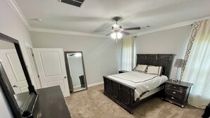 Un dormitorio con cama, mesita de noche, cómoda, ventilador de techo y espejo.