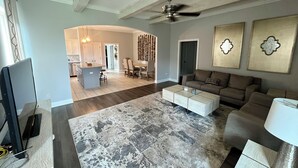 Un salón espacioso con un tapete grande color gris, un ventilador de techo y un sofá moderno.