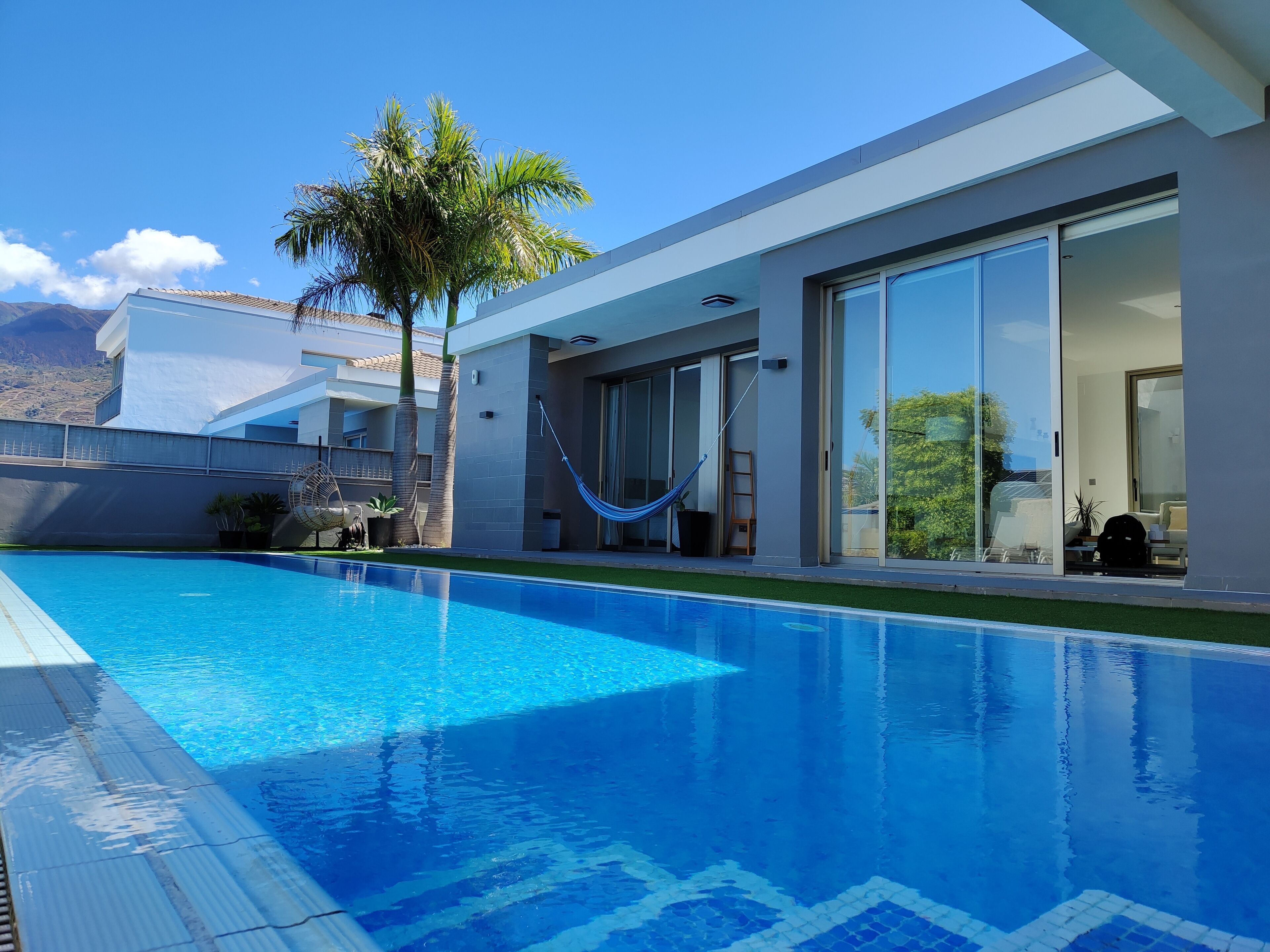 A modern house with a swimming pool, large sliding glass doors, and a hammock.