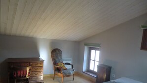 Ein Zimmer mit Holzboden, einem Bett, einem Sessel, einer Kommode und einem Fenster.