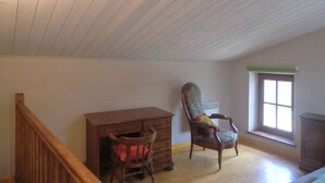 Ein Zimmer mit schrägen Wänden, einem Holztisch, einem Stuhl und einem Fenster mit Blick.
