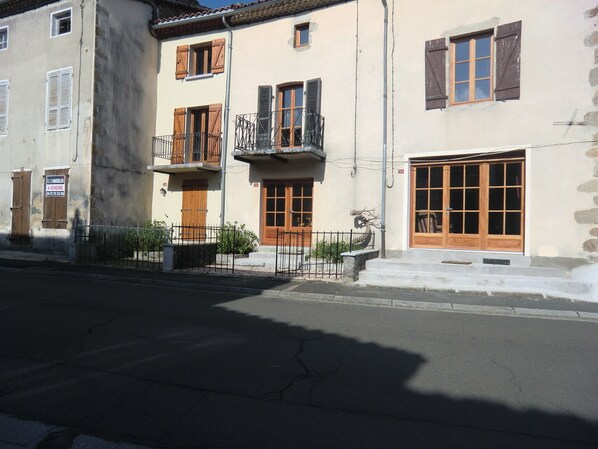 A two-story building with wooden shutters, a balcony, and a large window.