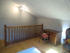 A room with a sloped ceiling, wooden desk, chair, and a dresser.