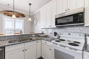 A kitchen with white cabinets, a granite countertop, a stainless steel oven, a microwave, and a clock on the wall.