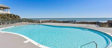 A clear blue swimming pool with a wooden deck, a lifeguard stand, and a view of the ocean.
