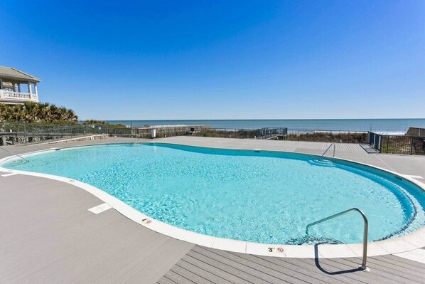 Una piscina azul cristalina con un muelle de madera, un puesto de socorrista y vistas al océano.