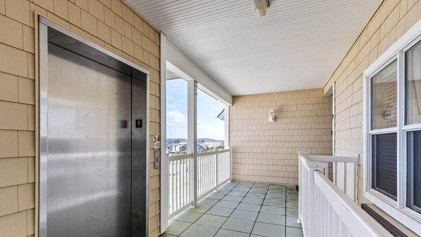 A covered balcony with a metal elevator door, tiled floor, and a view of the cityscape.