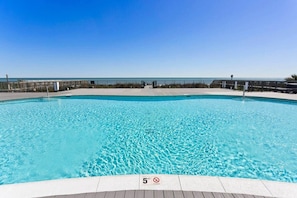 Ein klares, blaues Schwimmbecken mit Holzdeckrand, einem Metallzaun und wolkenlosem Himmel.