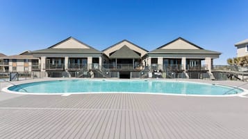 A poolside view of a hotel with a large swimming pool, outdoor deck, and three-story buildings with balconies.