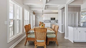A dining area with a glass-top table, wicker chairs, and a kitchen in the background.