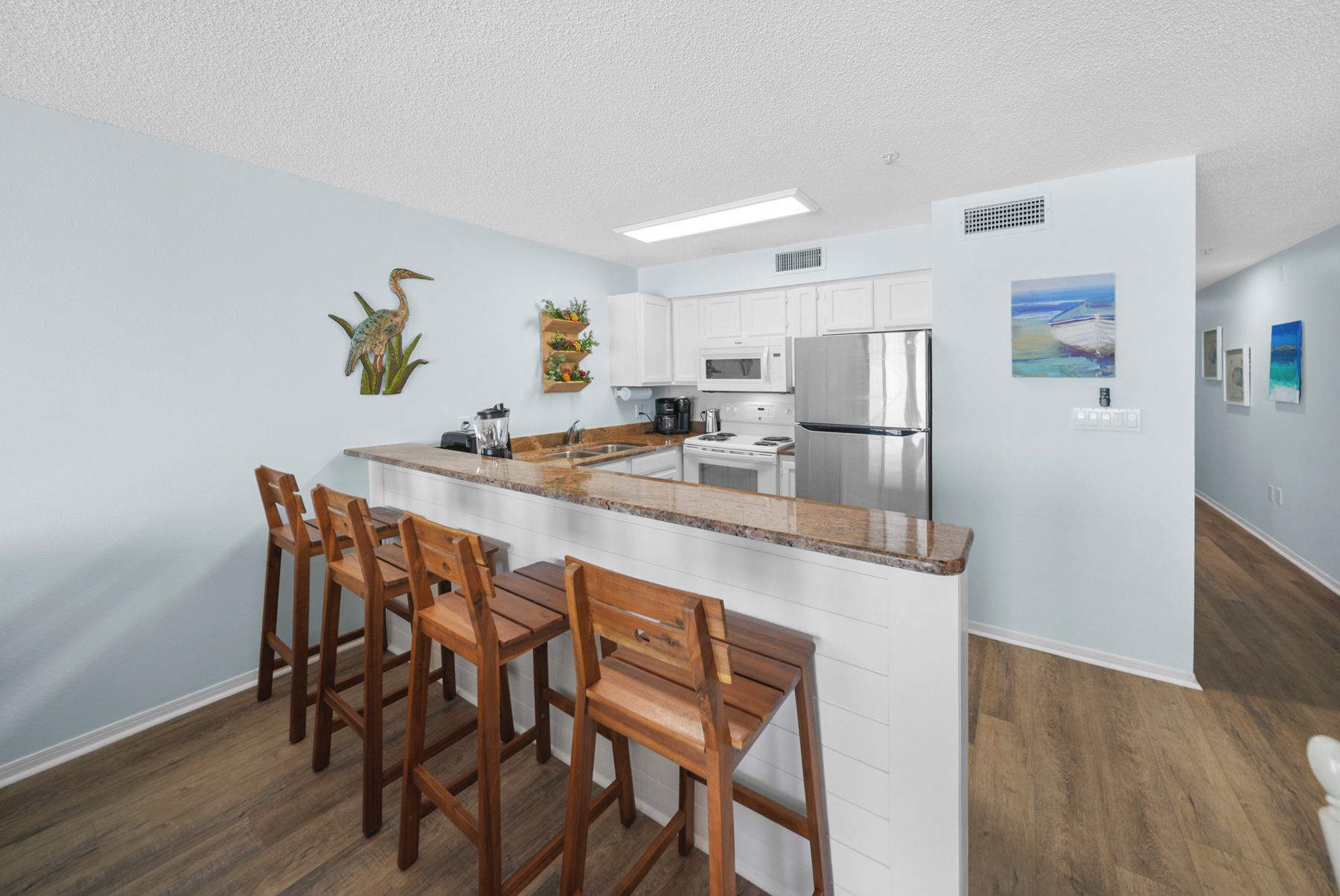 A modern kitchen with a central island, bar stools, white cabinets, stainless steel appliances, and artwork on the walls.
