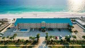 Um hotel com piscina central, v ários espaços de estacionamento e vista para a praia.
