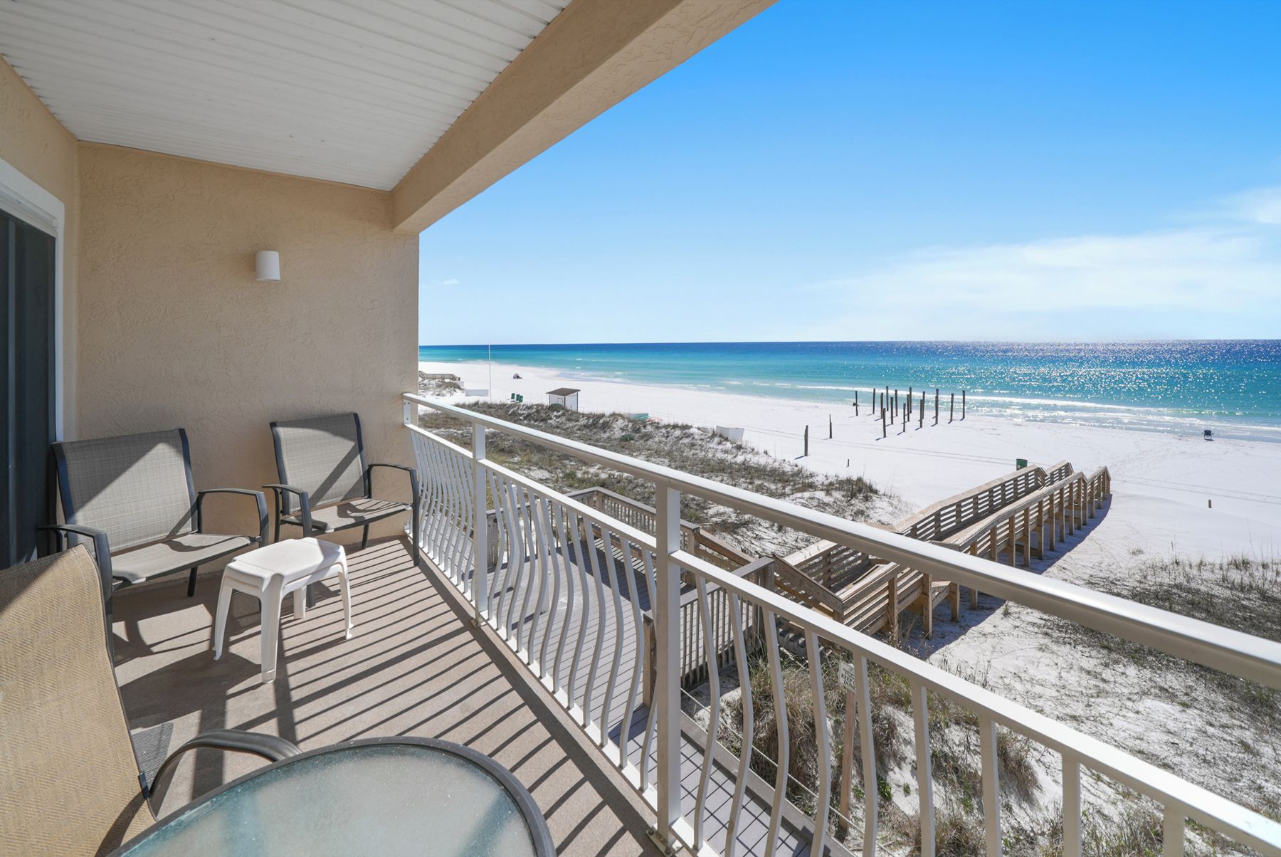 A balcony with outdoor seating, a view of a beach, and a wooden deck.