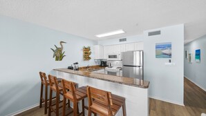 Uma cozinha moderna com ilha central, banquetas, armários brancos, eletrodomésticos de aço inoxidável e obras de arte nas paredes.