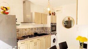 Ett modernt kök med ett kylskåp i rostfritt stål, träskåp, en inbyggd ugn, en tvättmaskin och en matplats med ett bord och stolar.