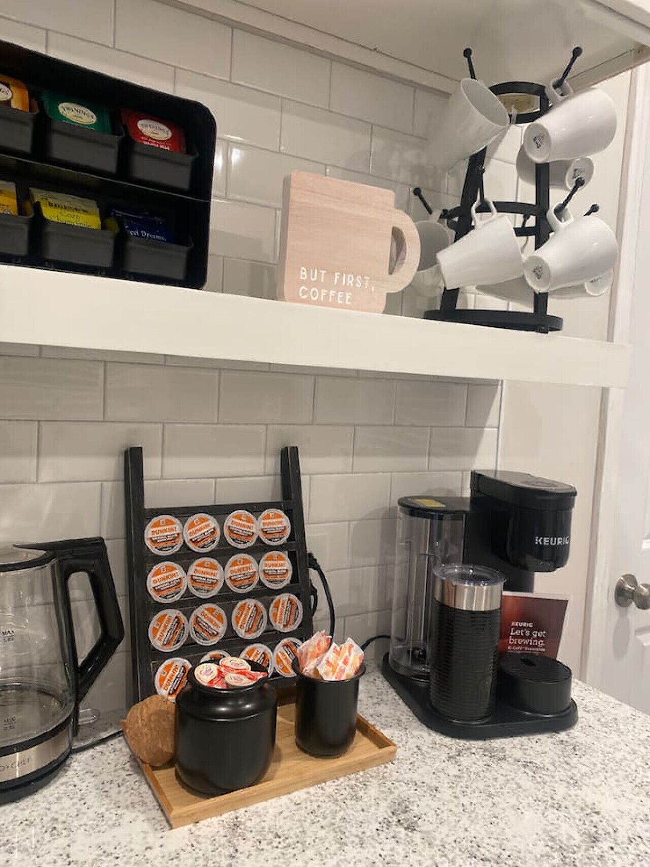 Et køkken med kaffestation, der indeholder en kaffemaskine, en bakke med kaffekapsler og et skilt med teksten "Men først, kaffe".