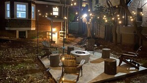 Une terrasse extérieure dotée d’un foyer, de sièges et de guirlandes lumineuses.