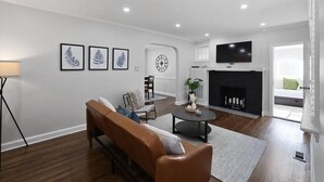 Un salon avec un canapé marron, une table basse ronde, une cheminée et un téléviseur fixé au mur.