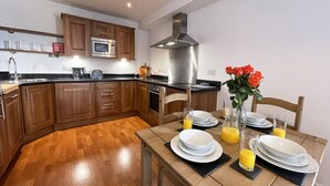 A modern kitchen with wooden cabinets, a stainless steel range hood, and a dining table set with plates, glasses, and orange juice.