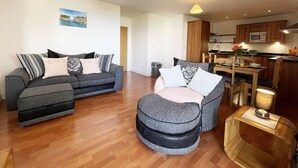 A modern living room with a grey sofa set, a round ottoman, and a dining area with wooden furniture.