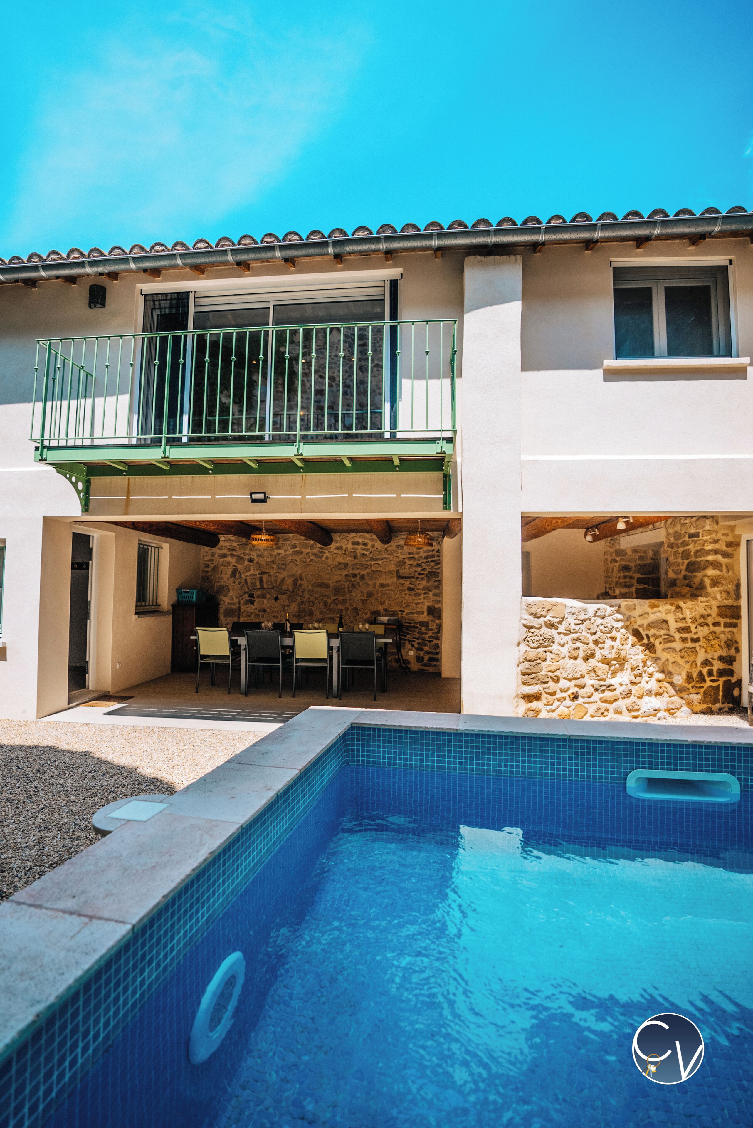 A two-story house with a swimming pool, outdoor seating, and a stone wall.