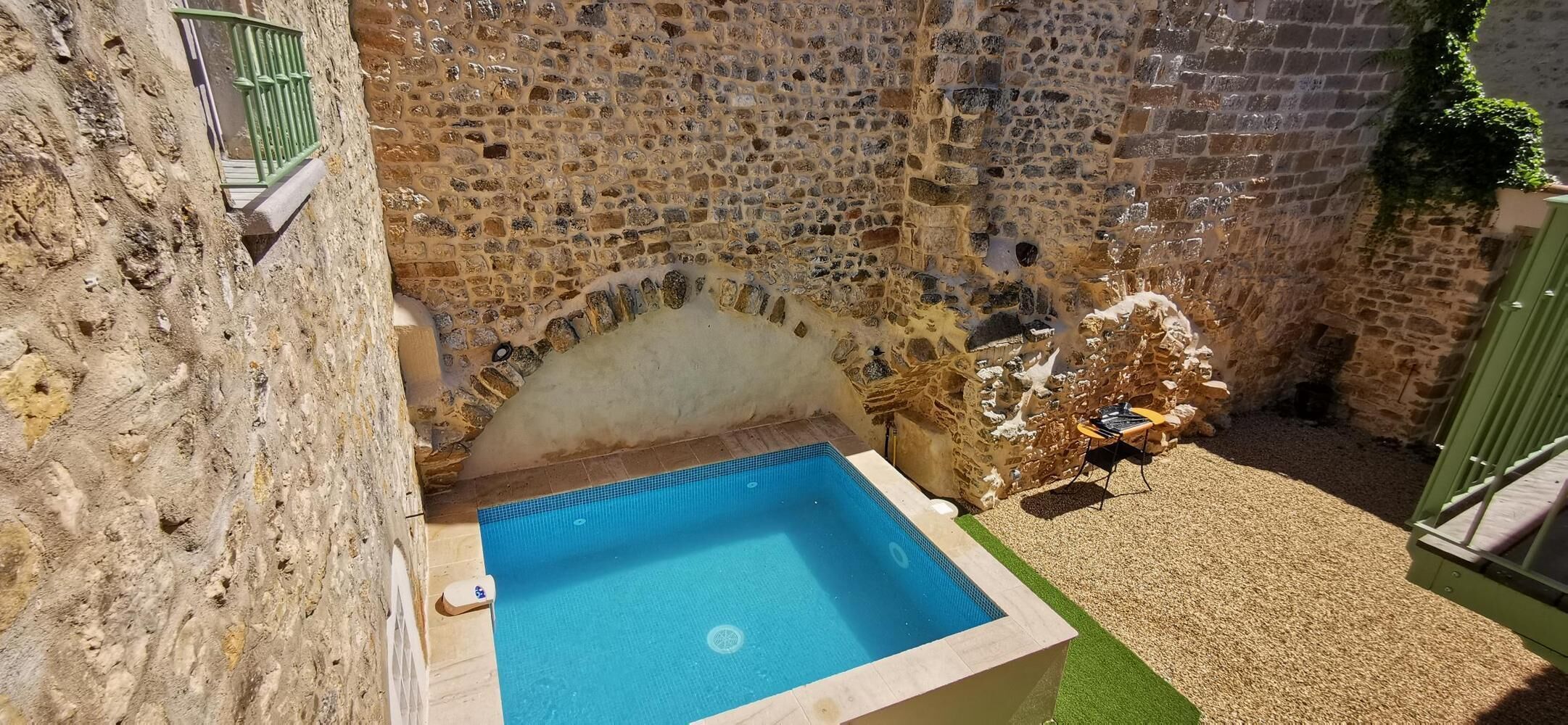 A stone-walled swimming pool with a small deck area and a grill.