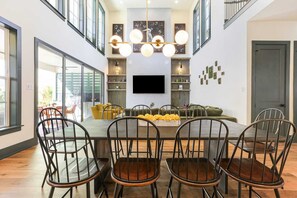 A dining area with a large table, chairs, a TV, and decorative wall art.