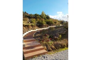 Un escalier extérieur en pierre menant au sommet d’une colline, entouré d’une végétation desséchée et sous un ciel dégagé.