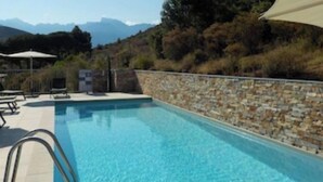 Une piscine bordée d’un muret en pierre, avec des chaises longues et des parasols.